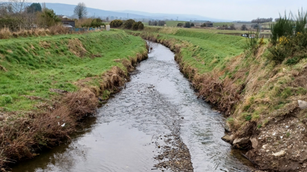 Shows a river with banks on either side and mountains in the background