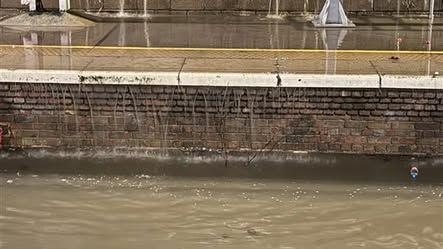 Flooded railway line with more gushing over the edge of the platform.