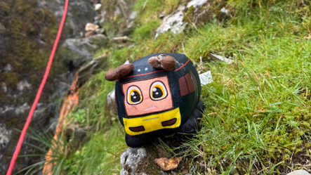 A black and yellow cuddly toy of a bus, sat on a grassy verge.