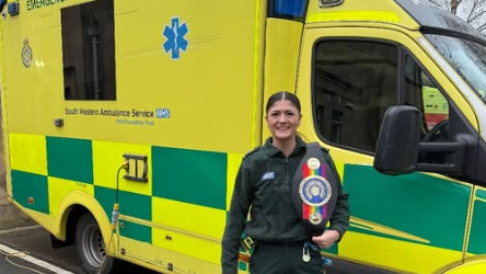 Megan in paramedic uniform standing in front of an ambulance holding her boxing title trophy