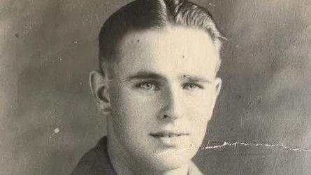 A black and white photograph of a 20-year-old Duncan Hilling in his military uniform sent home to his parents. It is a photo of his head. He has short hair with a middle parting, and is smiling at the camera. 
