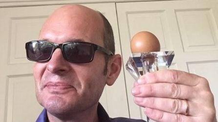 Bald man wearing sunglasses holding a round-shaped egg on a transparent stand.