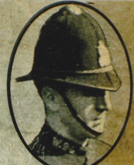 An old black-and-white photograph of a police officer, yellowed with age. He is wearing a traditional police helmet with a chin strap.