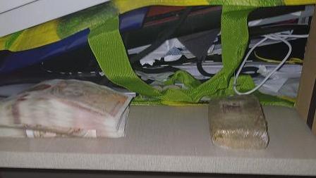 A pile of cash next to a package containing suspected drugs, surrounded by other household paraphenalia. 