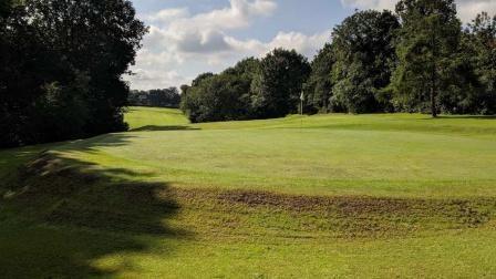 A golf course covered in green grass with green trees on the periphery. 