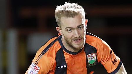 Callum Stead runs after the ball in his amber and black Barnet home shirt. He is looking down at the ball which is out of the picture.