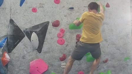 A man in a yellow t-shirt and grey shorts climbing without a harness on an indoor climbing wall