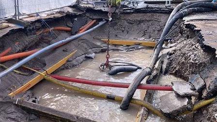 Site of burst main with pipes going into and across area that has been dug out but is full of muddy water.