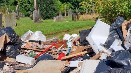 A large pile of rubbish and debris discarded at a cemetery.