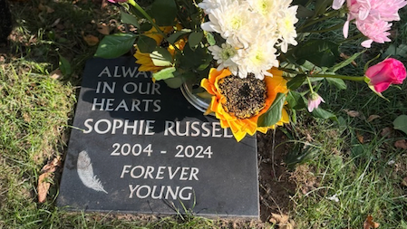 A plaque on the ground for Sophie Russell. It is surrounded by a bunch of flowers.