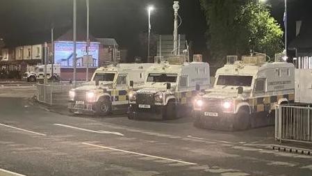 Three police Land Rovers parked with their lights on in Belfast's Broadway area