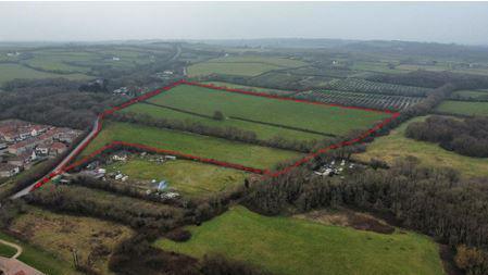 An aerial photo of a large patch of land that is square in shape with a thin section stretching off from one corner. The land is agricultural land with a large hedge running through the centre.