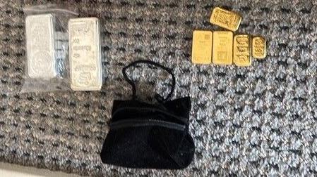 Five gold bullions and two silver bullions laid out. There is also a small black bag.