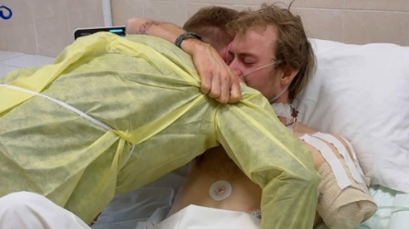 Eddy and one of his fellow volunteers in a hospital room in Ukraine. Eddy's shoulder is bandaged up after his arm was amputated. He is tightly hugging the fellow volunteer.