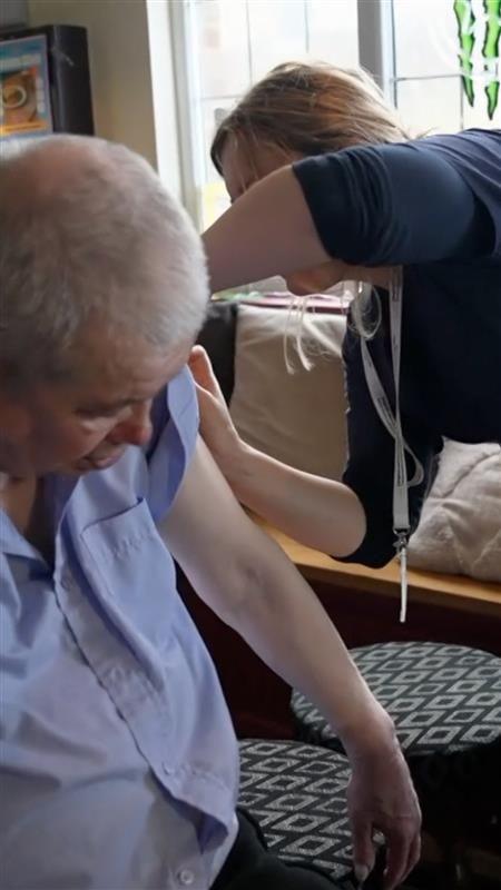 A man in a light, button-up shirt getting a jab from a person in a navy shirt.