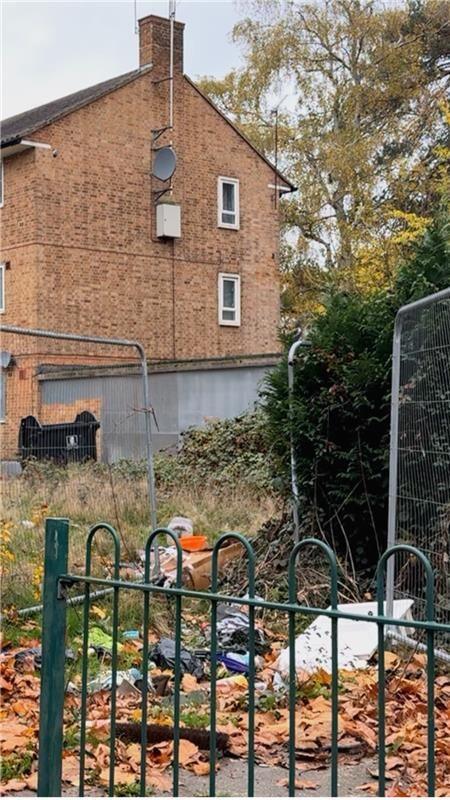 A brick building in the background and a green metal gate with litter behind it in the foreground.