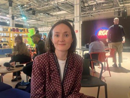 Gaby Jenks sitting in a communal area of the Aviva Studios wearing a dark red and white patterned blazer