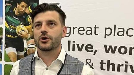 Thomas Manning with short dark hair and beard wearing a grey waistcoat and light-coloured shirt smiling at the camera.