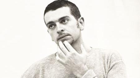A black and white photo of a younger Geoff Hopson who has dark short hair and has his fingers on his chin looking thoughtful.