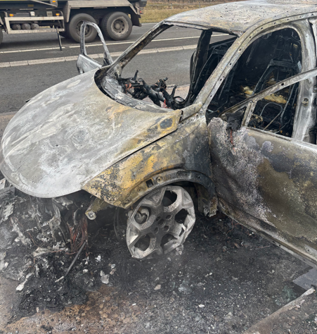 Makina e bardhë është dëmtuar plotësisht nga zjarri. Të gjitha xhamat janë thyer dhe ka mbeturina përreth automjetit.