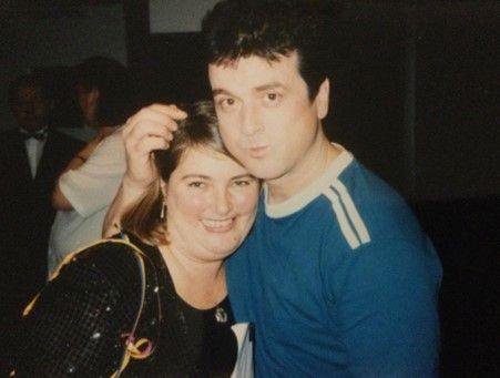 Gail stands beside band member, Les McKeown. She leans into him with her arm around him and his arm is around her shoulders. Gail smiles and Les is pouting. Les wears a blue t-shirt and Gail has on a black blouse. 