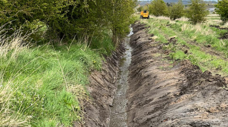 A trench with lots of muddy water next to a disused railway track 