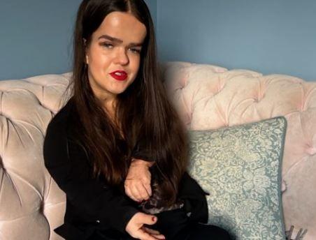 Woman with long brown hair and red lipstick sat on a pink sofa