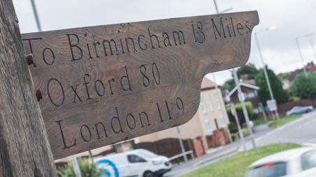 A wooden fingerpost which lists the distances to Birmingham, Oxford and London.