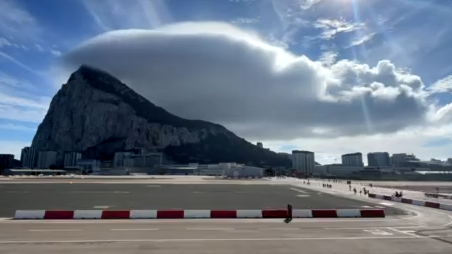 View of the Rock of Gibraltar from Gibraltar International Airport with a dense white cloud to one side on an otherwise sunny day