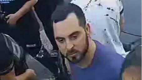 A man with short brown hair, stubble and a blue t-shirt in a crowd. 