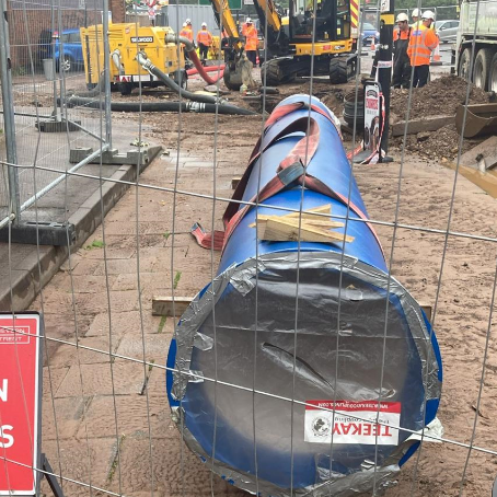 A large new blue pipe sitting on top of a road behind a metal fence