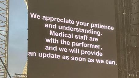A sign with a black background and white lettering reads: We appreciate your understanding. Medical staff are with the performer, and we will provide an update as soon as we can.