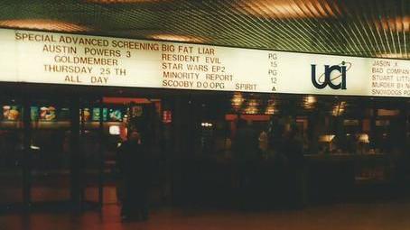 A dark cinema lobby with a big screen advertising films