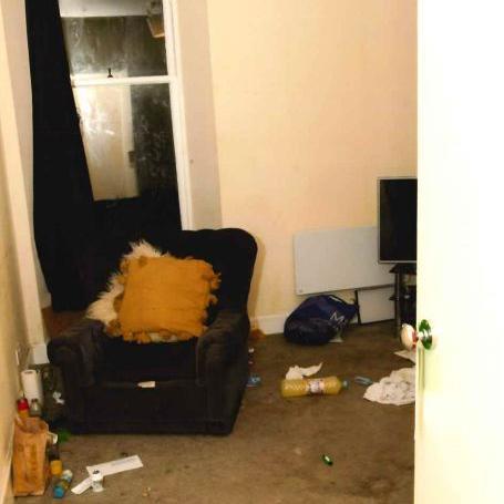 Tattered cushions on a dark armchair inside the dingy flat on Bright Street, Dundee. Debris, including a large bottle of Fanta, can be seen on the heavily stained carpet.