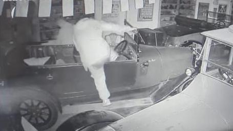 Black and white CCTV footage shows a suspect appearing to kick one of the classic cars