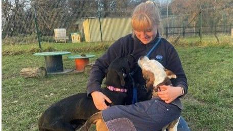 Katie is wearing her RSPCA fleece holding two dogs. She is sitting outside in a grassed and fenced in area