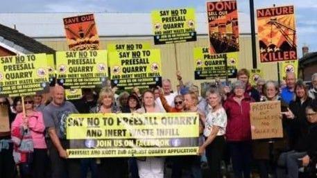 Dozens of people hold up yellow and black banners and placards with the words "Say no to Preesall Quarry and inert waste infill".
