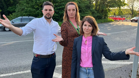 A man and two women standing with their hands out near a road