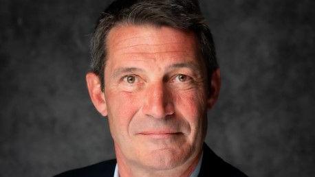 Head and shoulders image of Oliver Lee, a man with dark grey hair looking at the camera in front of a grey background.