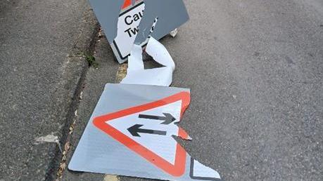 Damaged road signs on the road after being tampered with. The sign appears to be a two-way road sign with arrows pointing in opposite directions.