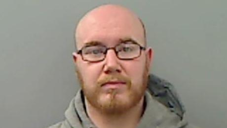 Mugshot of a bald man with glasses and a short ginger beard