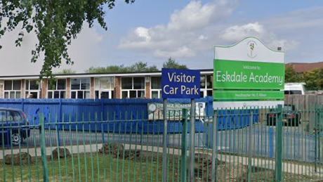 The visitor car park for Eskdale Academy in Hartlepool. A blue fence runs along the boundary of the school and cars can be seen parked inside.