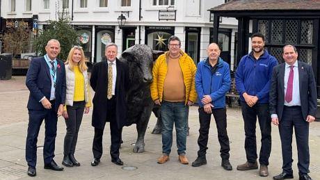 A group of people stand next to a statue of a bull and smile at the camera