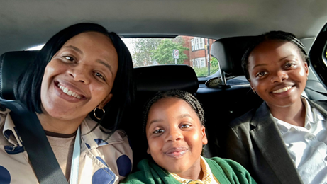 A mum in a car, alongside her two daughters. They are all smiling. 