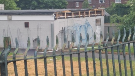 A single storey grey building, with graffiti on the walls, and the edge of the roof exposed on one side.