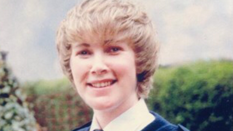 An old photo of a young female police officer in uniform, smiling at the camera. She has medium-length blonde hair with a fringe. She is stood outdoors with a hedge behind her. 