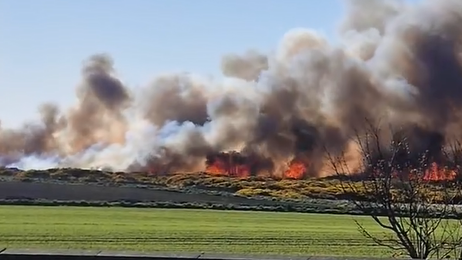A large fire across a field with lots of grey smoke in the sky