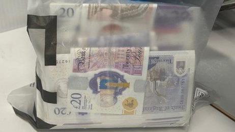 A wodge of £20 notes in a clear plastic bag is held up for the picture.