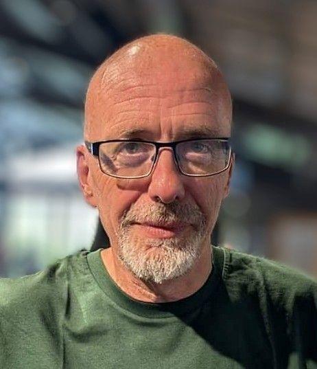 A bald man with glasses and a white beard looking into the camera and smiling