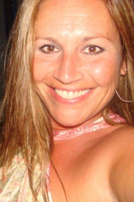 Victoria smiling while looking at the camera. She has long brown hair and wears hoop earrings. 